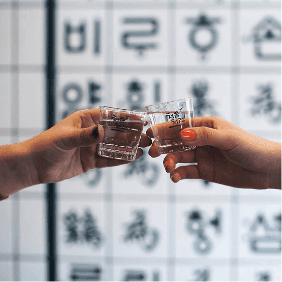 Two people touching small soju glasses together in a toast